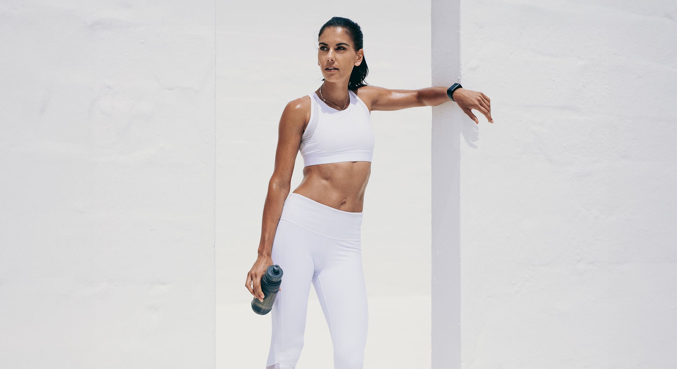 woman in white exercise clothes leaning against a wall